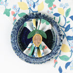 Botanical print cloth napkin placed in a blue textured bowl with a woven lemon napkin ring.