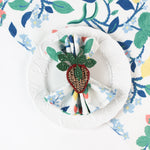 Botanical print cloth napkin styled on a white plate with a woven strawberry napkin ring.