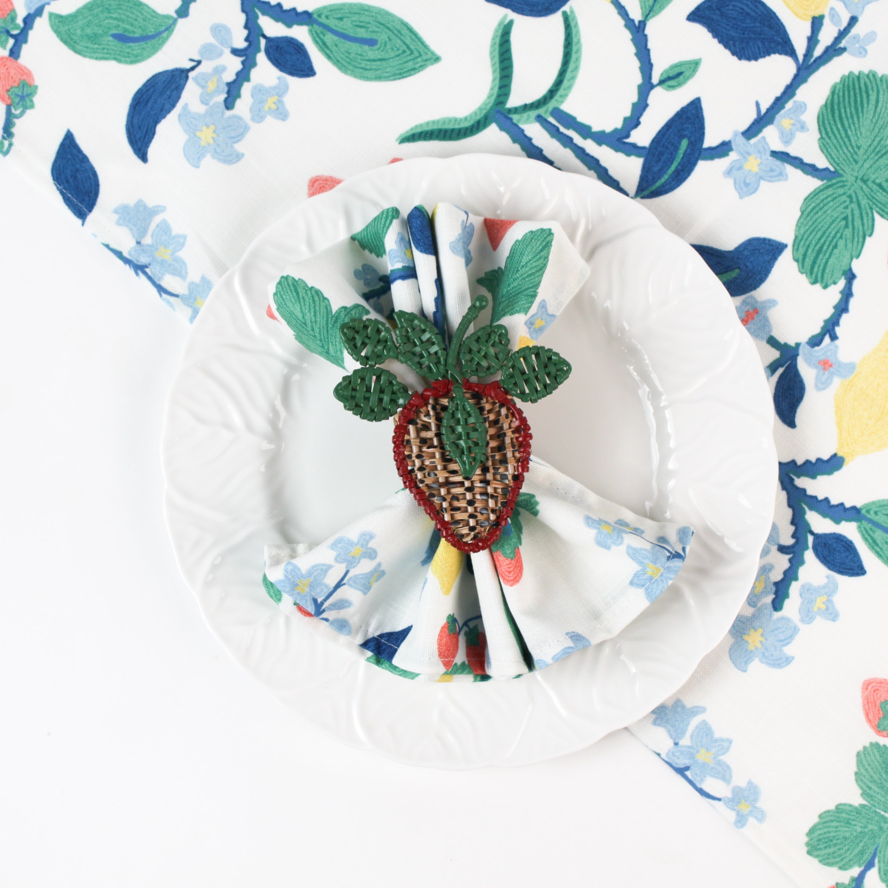 Botanical print cloth napkin styled on a white plate with a woven strawberry napkin ring.