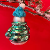 The reverse side of a glass snowman christmas ornaments. The snowman wears a blue jacket and hat. 
