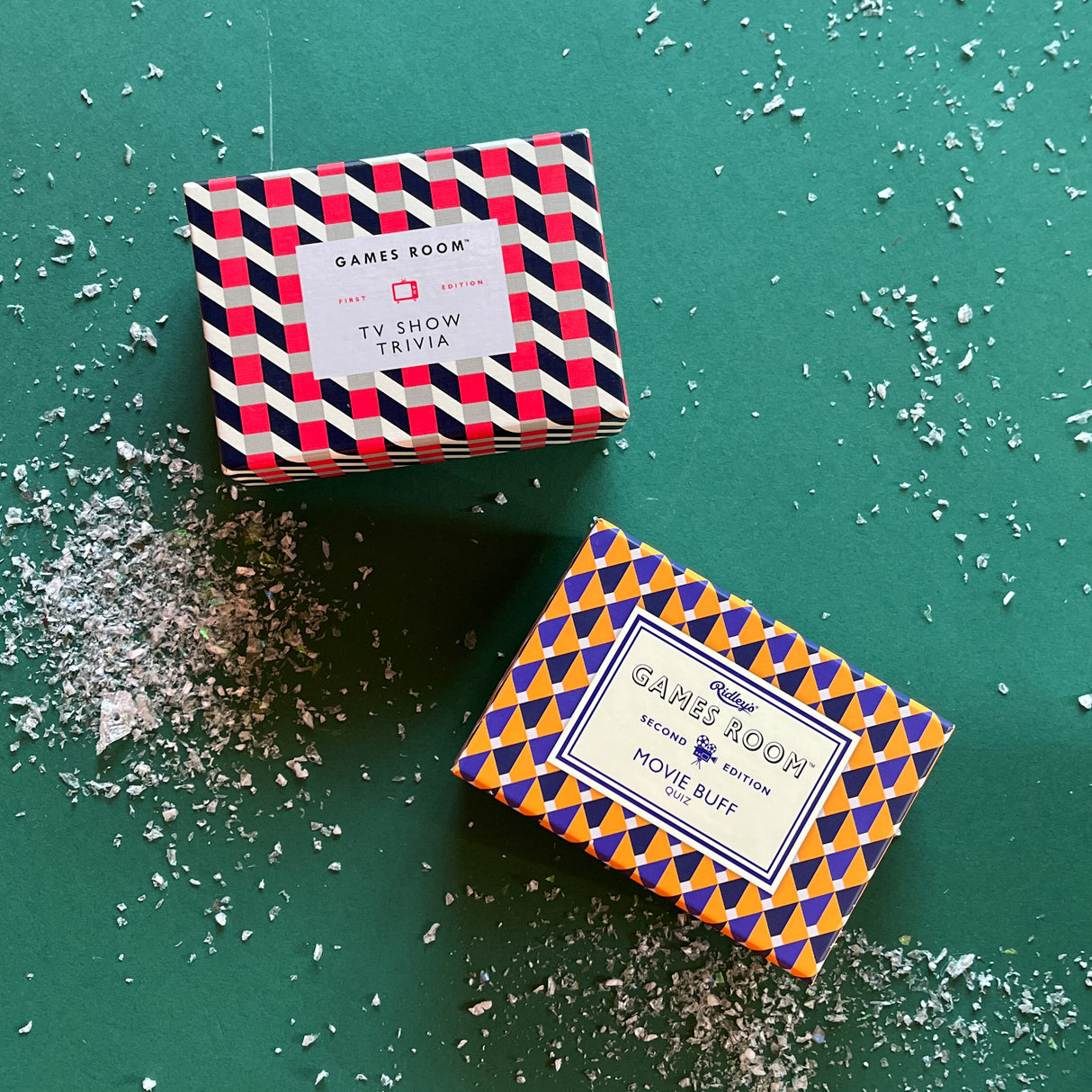 Two trivia game boxes with geometric patterns. One box is red with white text and the other is blue with yellow text, both with the title 'GAMES ROOM' and different game names visible.