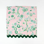 Pink cloth napkin featuring a green chinoiserie floral pattern with dark green scalloped trim.