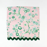 Pink cloth napkin featuring a green chinoiserie floral pattern with dark green scalloped trim.