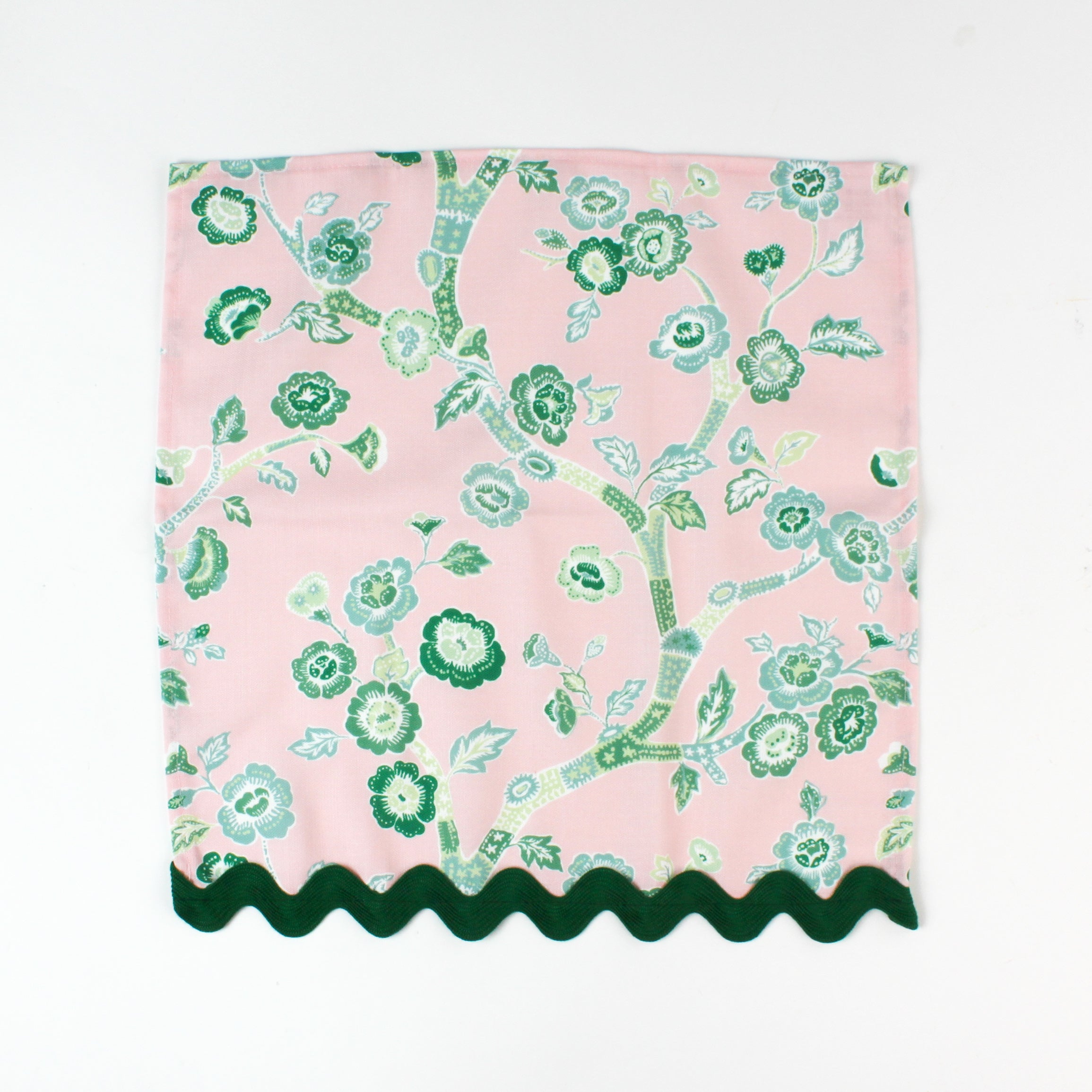 Pink cloth napkin featuring a green chinoiserie floral pattern with dark green scalloped trim.