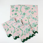 Set of pink cloth napkins with green chinoiserie floral print and dark green scalloped trim.