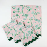 Set of pink cloth napkins with green chinoiserie floral print and dark green scalloped trim.