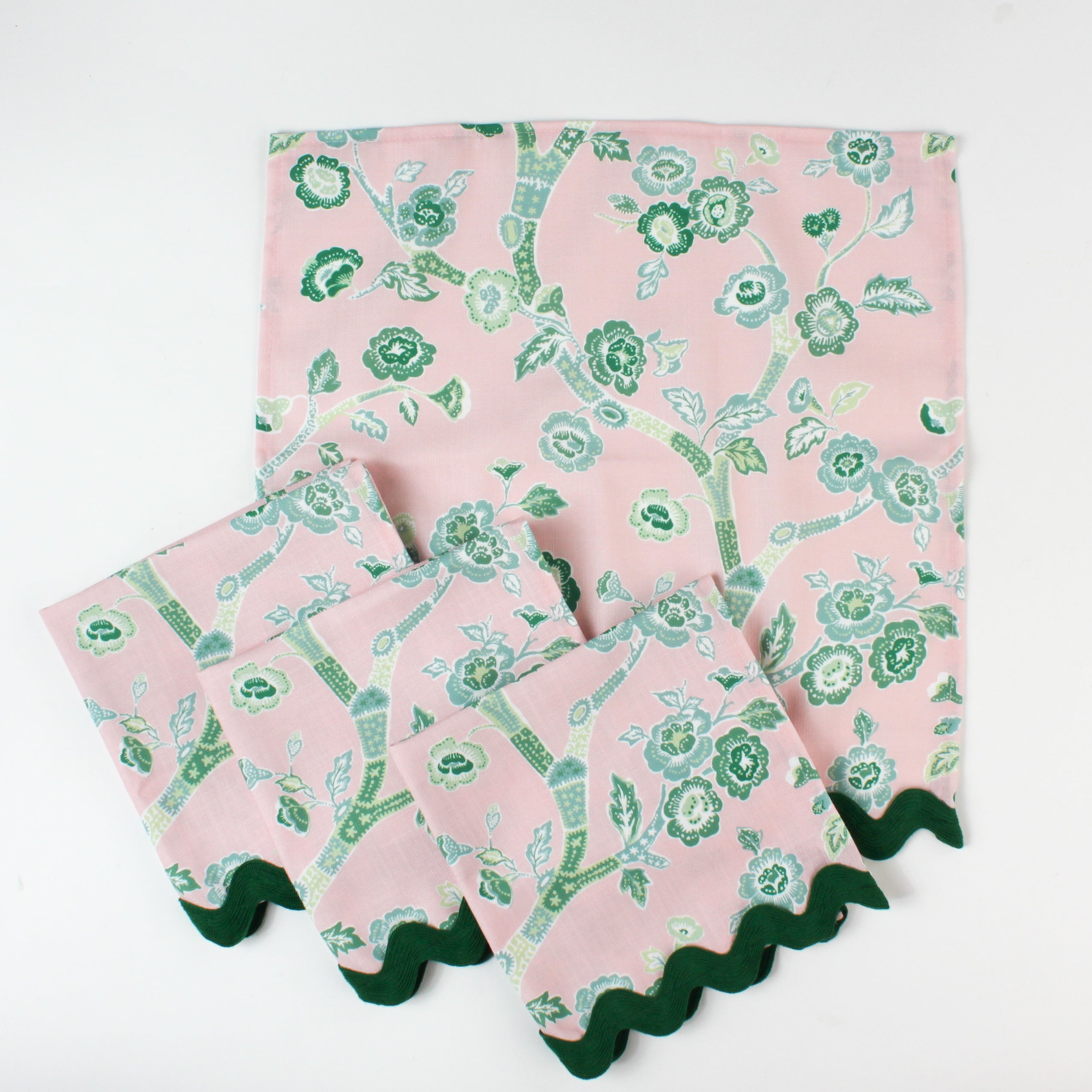 Set of pink cloth napkins with green chinoiserie floral print and dark green scalloped trim.