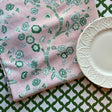 Temple Garden is a pink and green chinoiserie tablecloth with a white plate resting on the tablecloth on a green and white table