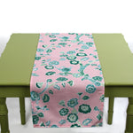Pink table runner with green floral pattern displayed on a green table.