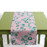 Pink table runner with green floral pattern displayed on a green table.