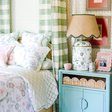A canopy bed with chinoiserie bedding next to a blue nightstand and chinoiserie lamp