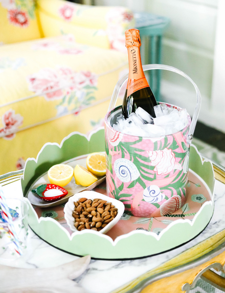 a pink and green chinoiserie tray filled with small snack dishes and an acrylic ice tray filled with champagne. 