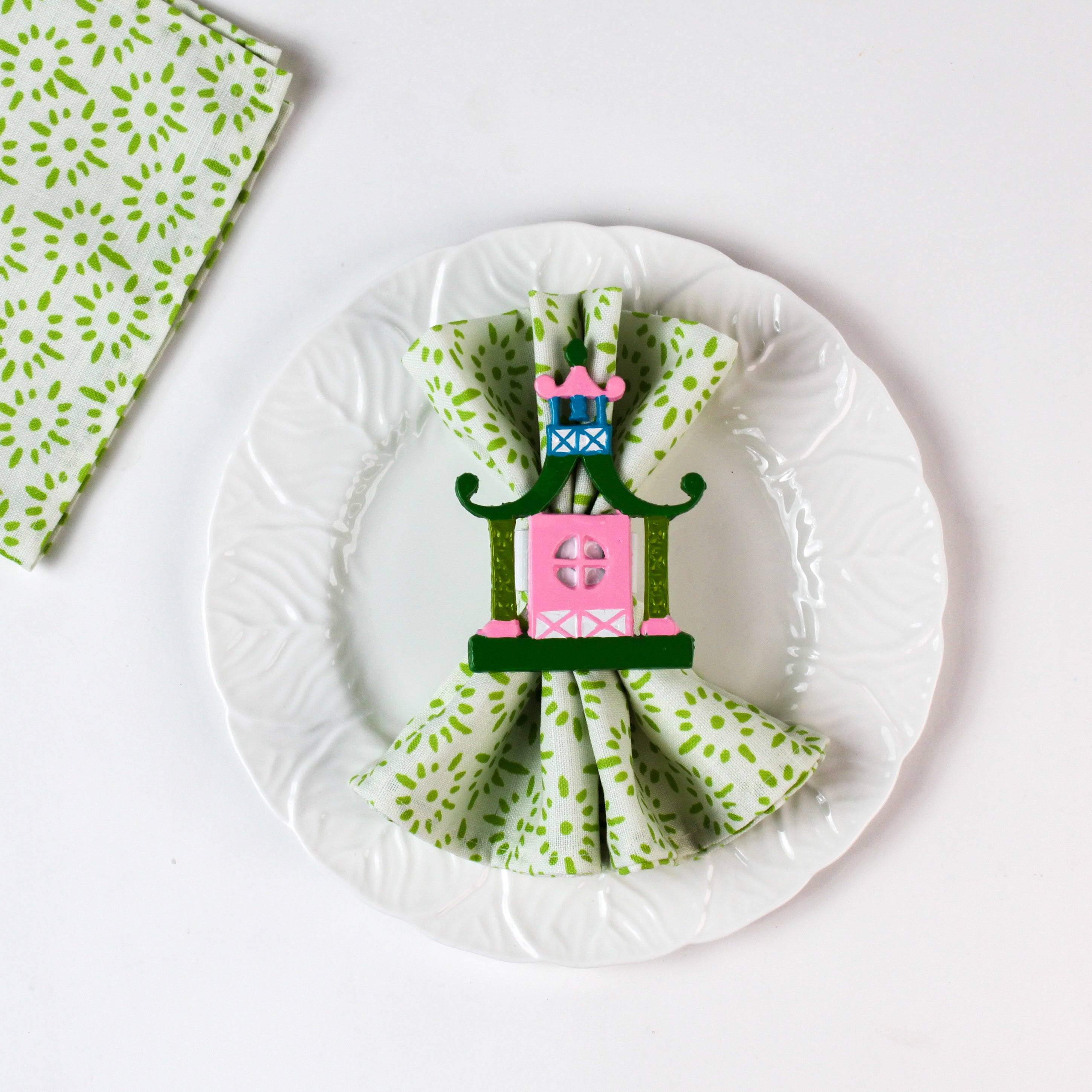 Green patterned cloth napkin styled on a white plate with a decorative pagoda napkin ring.