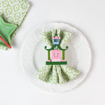 Green patterned cloth napkin displayed on a white plate with a pink and green pagoda napkin ring.
