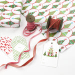 Twinkle Trees Christmas wrapping paper styled with gift tags, ribbon spools, and pink velvet ribbon.