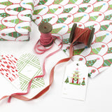 Twinkle Trees Christmas wrapping paper styled with gift tags, ribbon spools, and pink velvet ribbon.