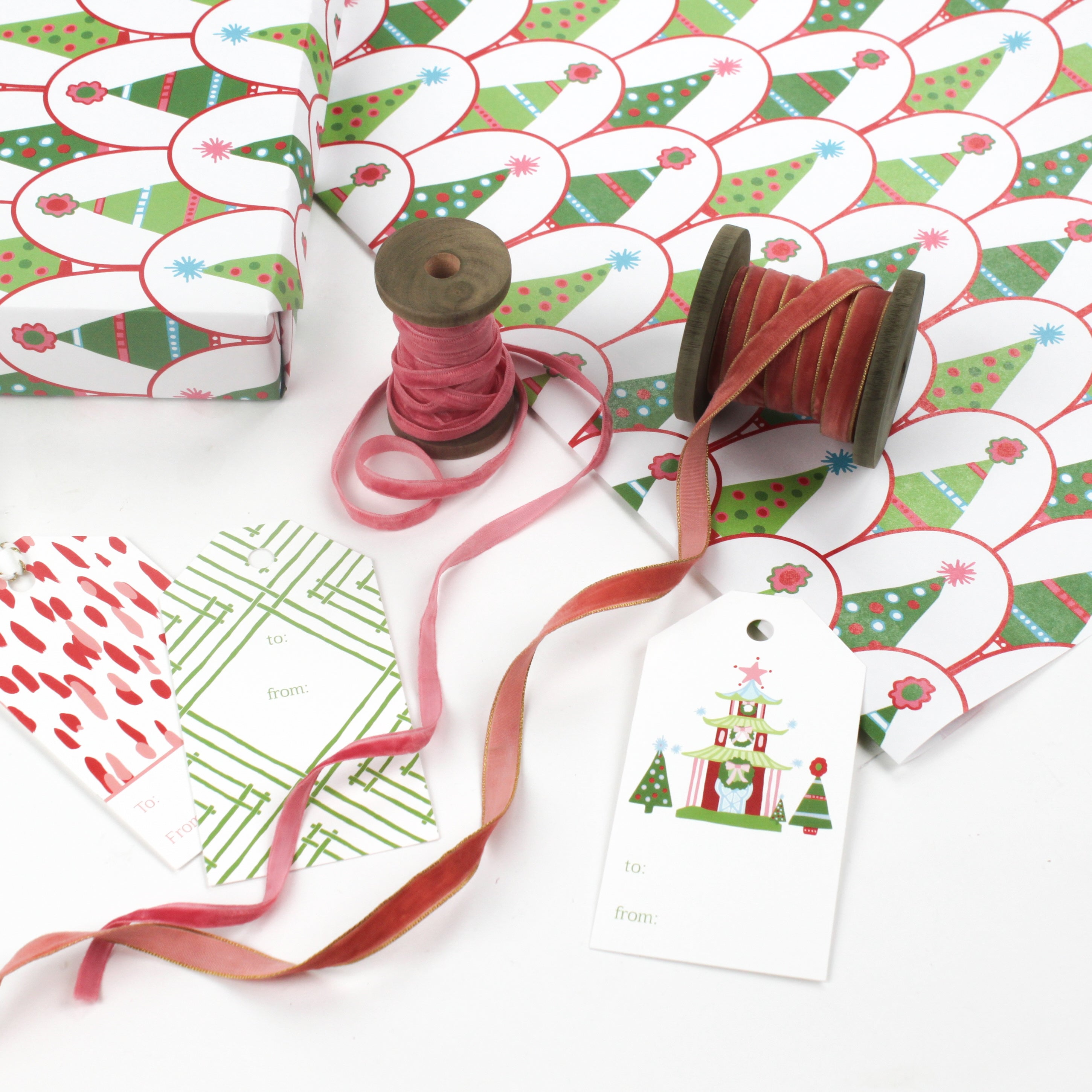 Twinkle Trees Christmas wrapping paper styled with gift tags, ribbon spools, and pink velvet ribbon.
