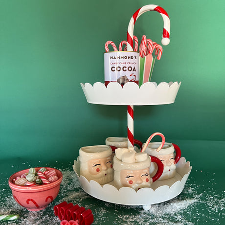 Two-Tier Tole Metal Decorative Candy Cane Centerpiece holding Santa mugs and a tin of cocoa