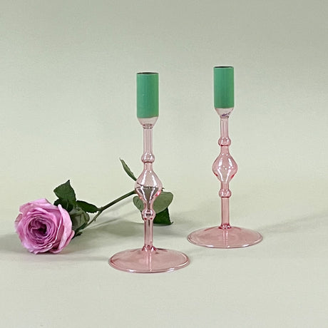two pink colored glass candle holders with green tops with a pink rose