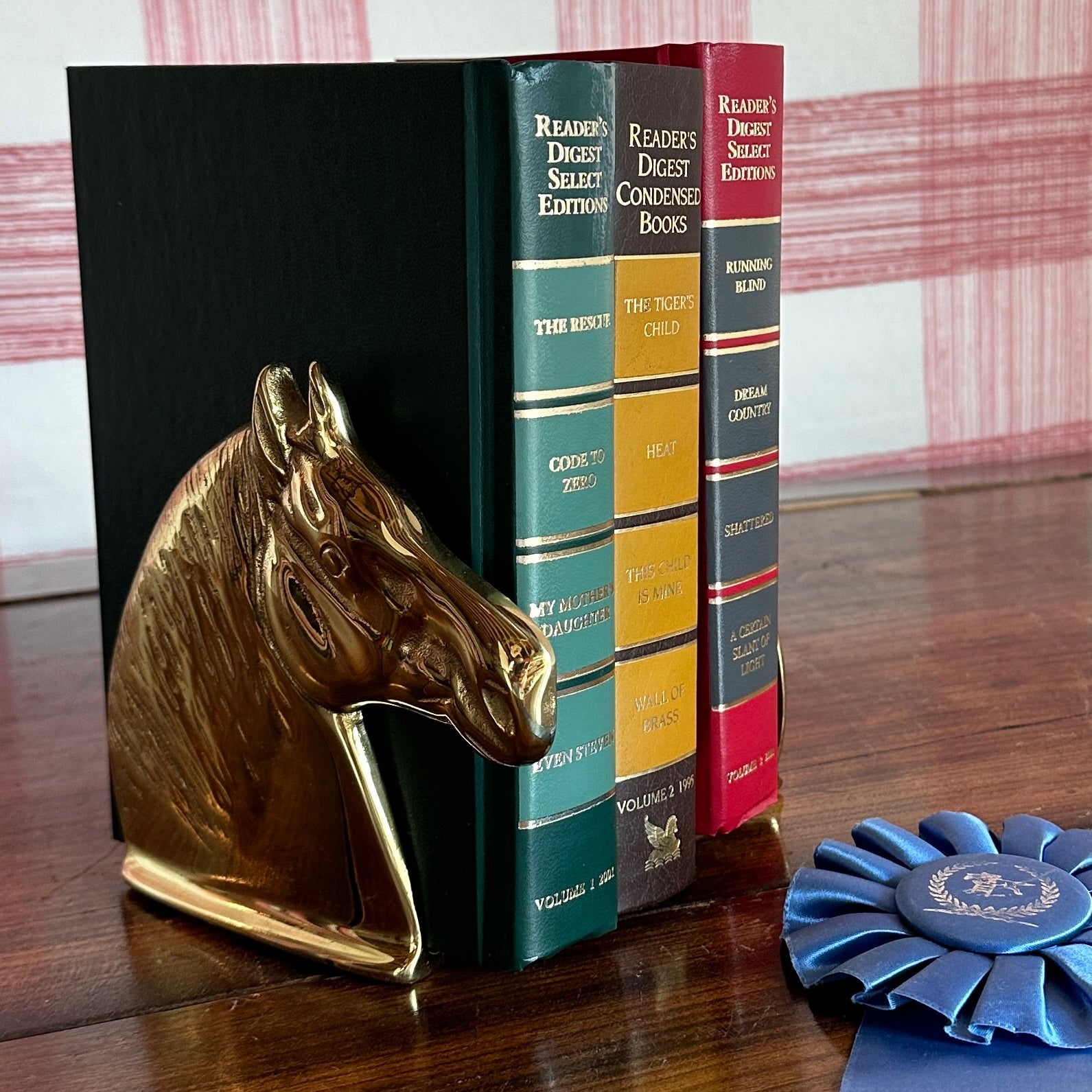brass horse book ends with three hardback books between them and a blue rosette in the foreground.