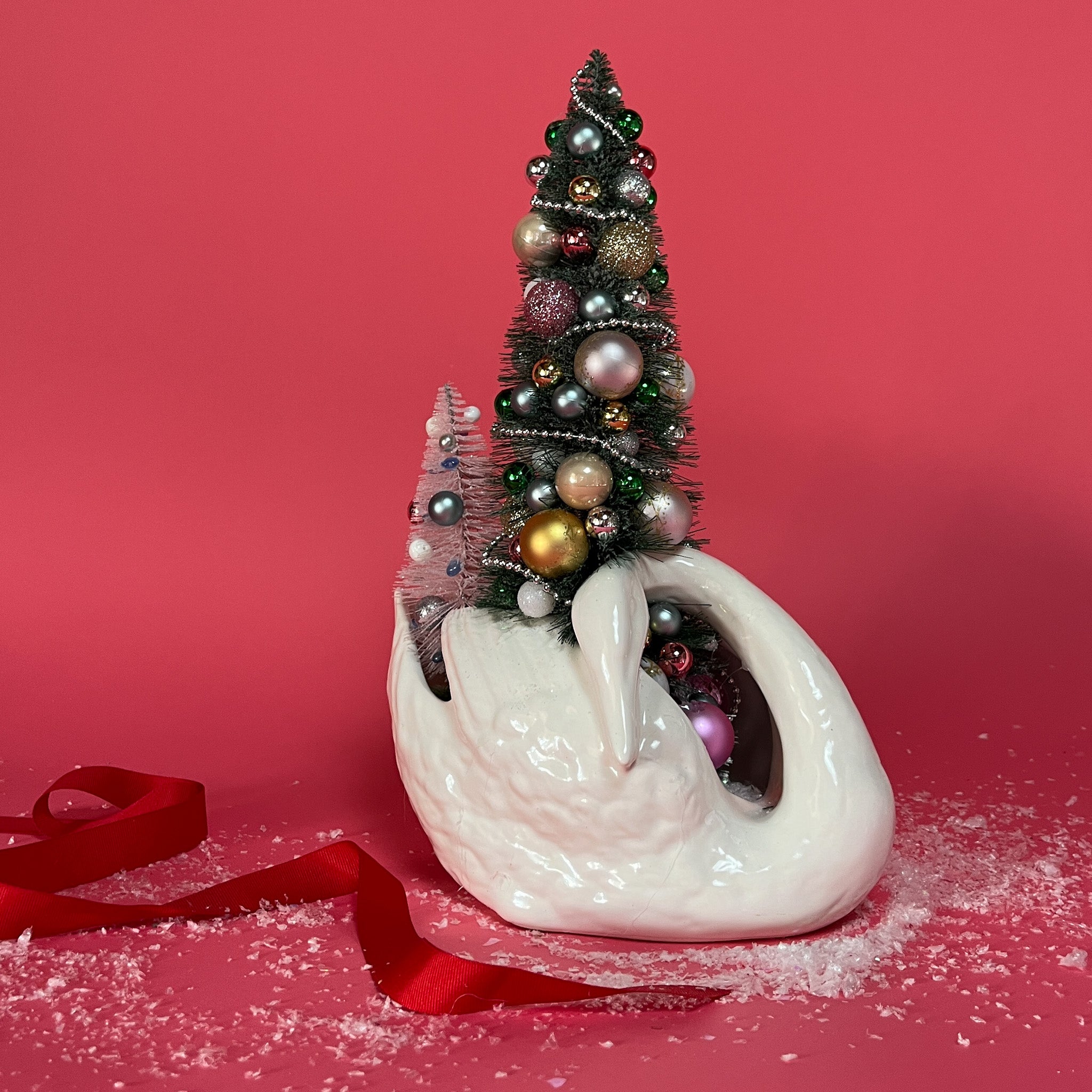 a white Vintage Arched-Neck Ceramic Swan w/ a Pink/Purple/Gold Christmas Tree inside it against a red background. 