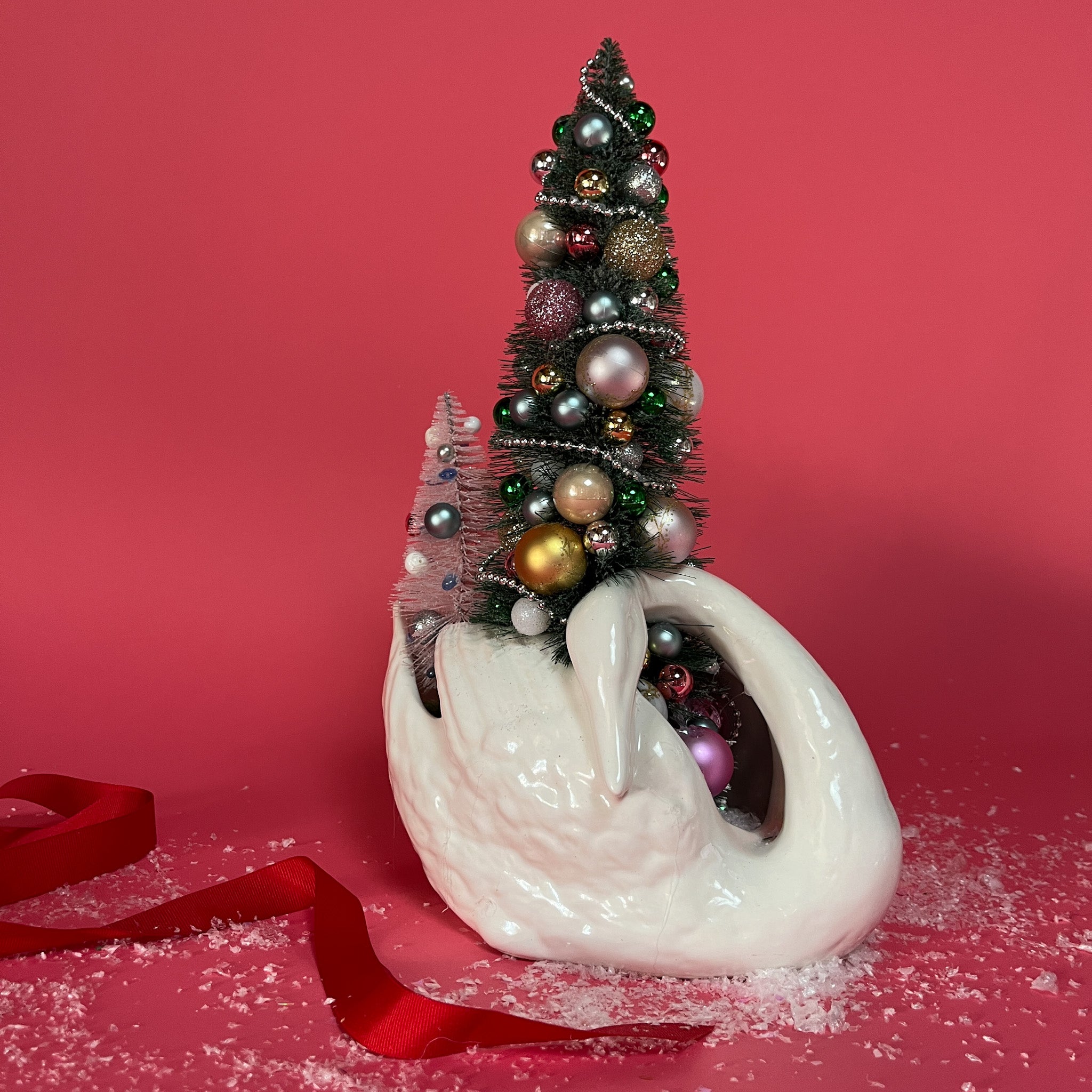 a white Vintage Arched-Neck Ceramic Swan w/ a Pink/Purple/Gold Christmas Tree inside it against a red background. 
