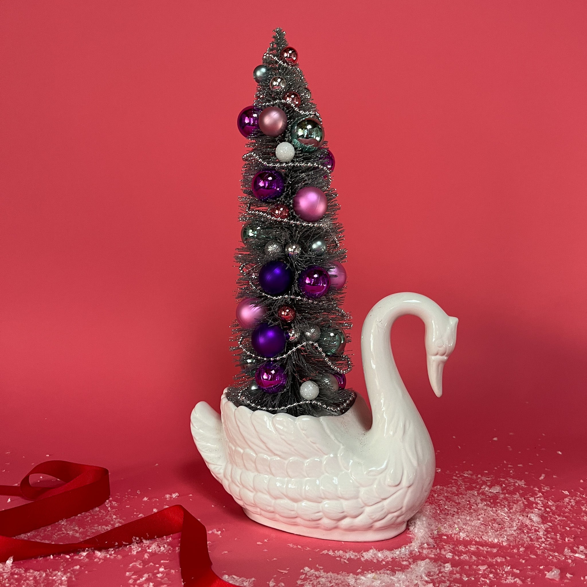 a white Vintage Arched-Neck Ceramic Swan w/ a Pink/Purple/Silver Christmas Tree inside it against a red background. 