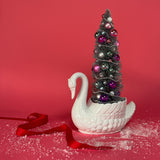 a white Vintage Arched-Neck Ceramic Swan w/ a Pink/Purple/Silver Christmas Tree inside it against a red background. 