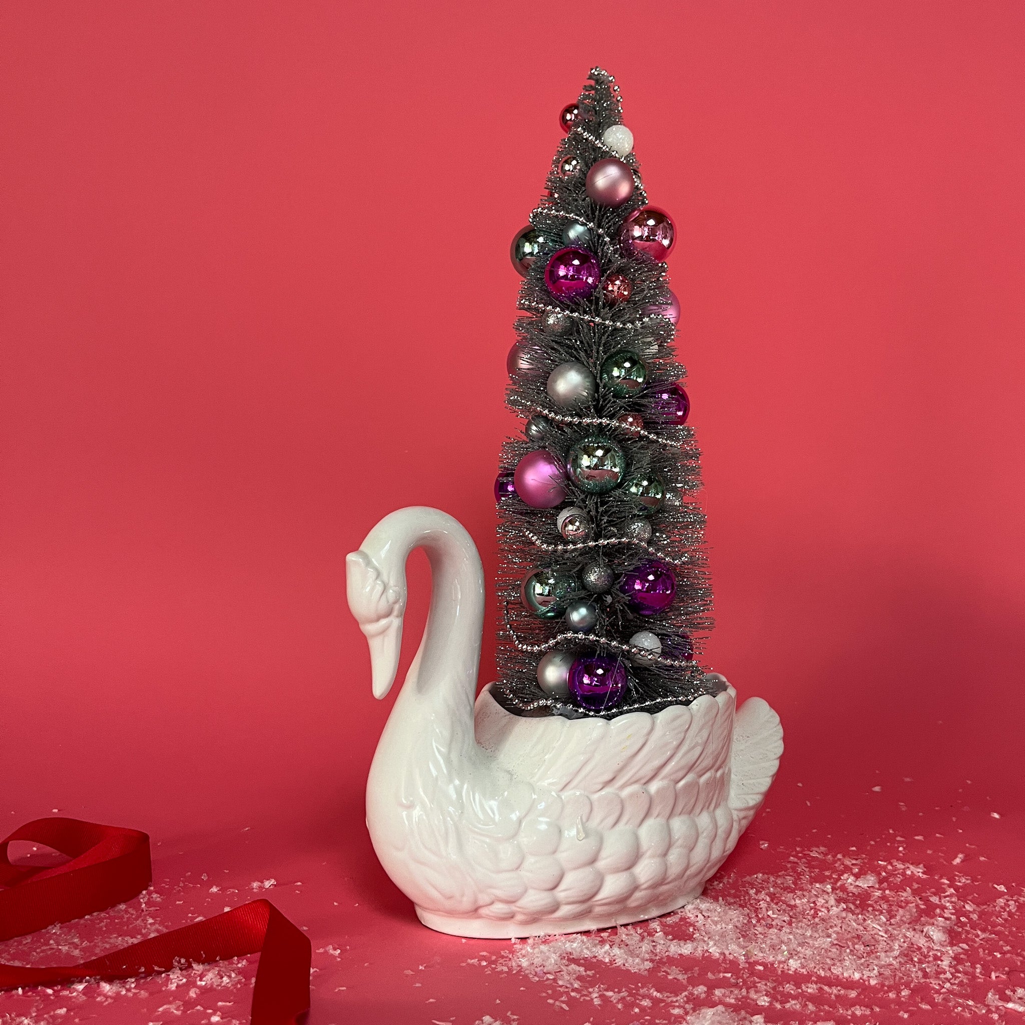 a white Vintage Arched-Neck Ceramic Swan w/ a Pink/Purple/Silver Glitter Christmas Tree inside it against a red background. 