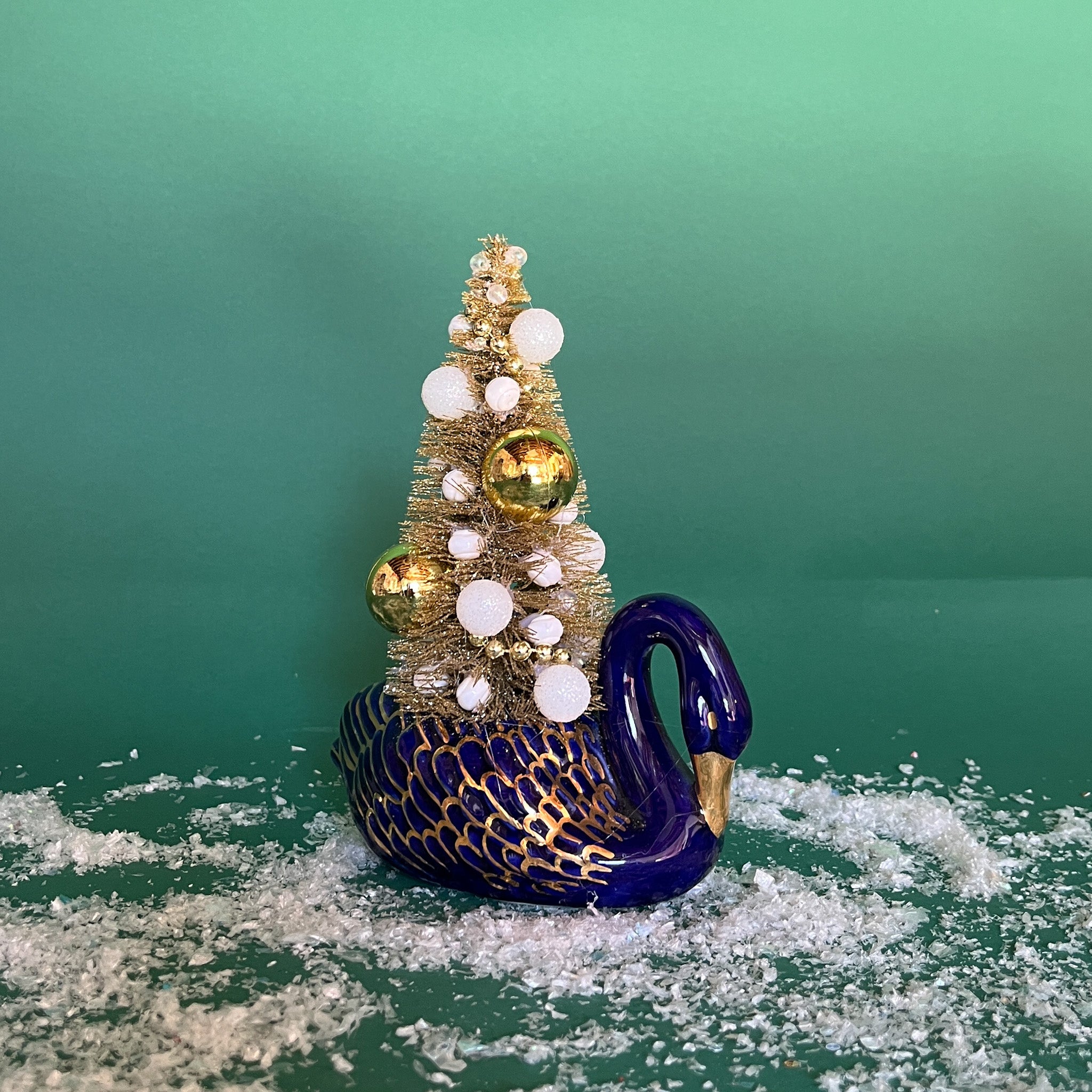 a Vintage Blue/Gold Ceramic Swan w/Gold Christmas Tree Centerpiece against a green background. 