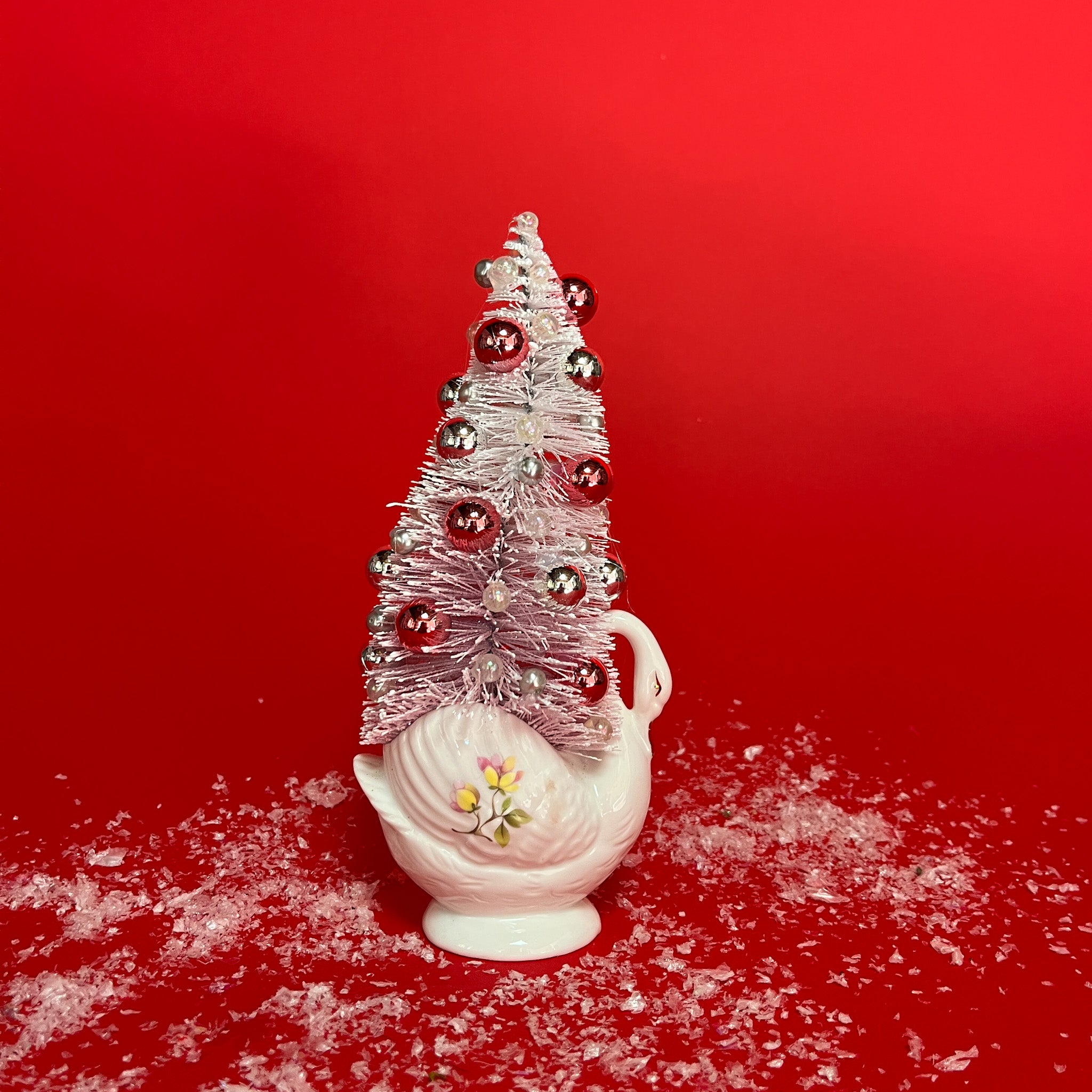 a white floral Vintage Ceramic Swan w/ Flocked Christmas Tree Centerpiece against a red background. 