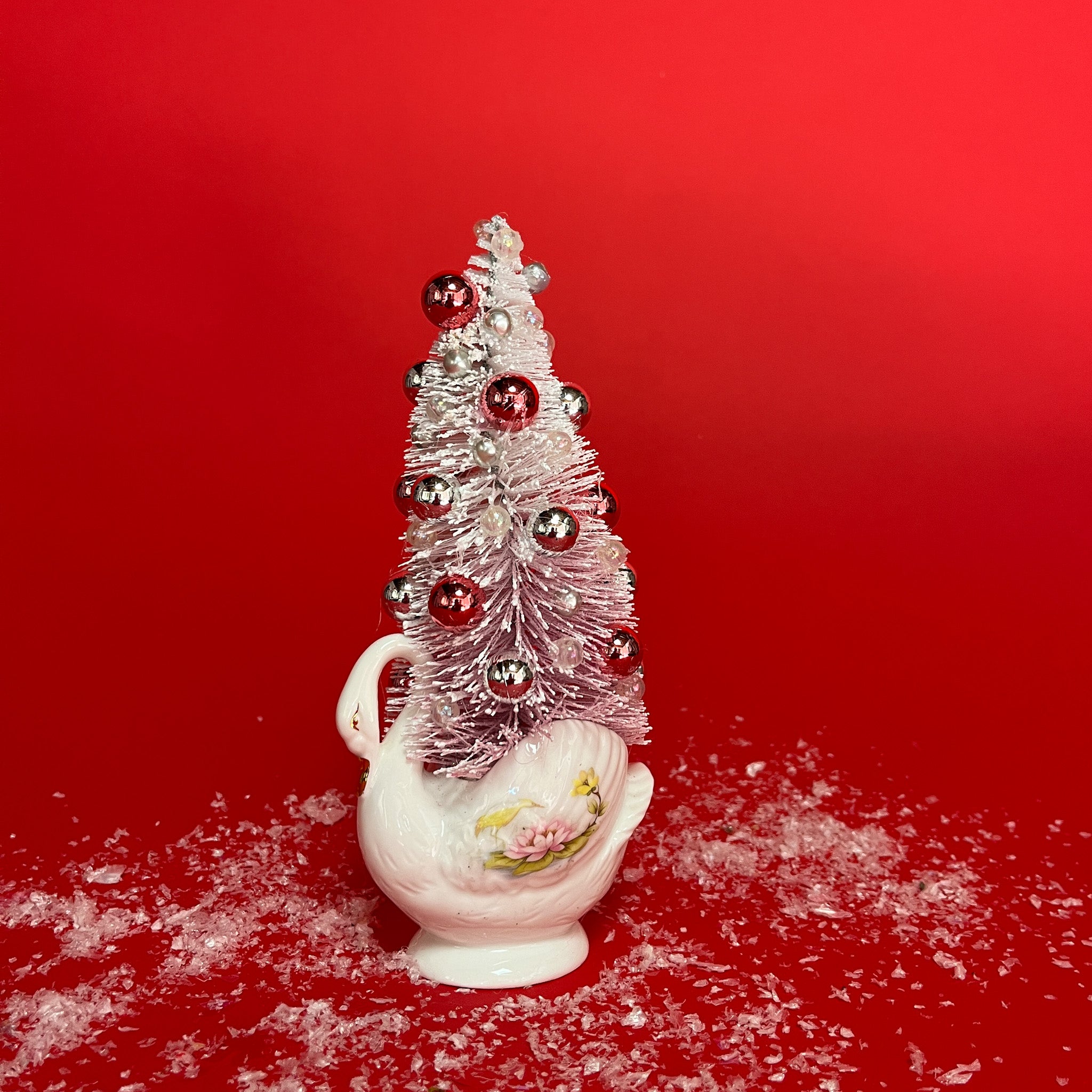 a white floral Vintage Ceramic Swan w/ Flocked Christmas Tree Centerpiece against a red background. 