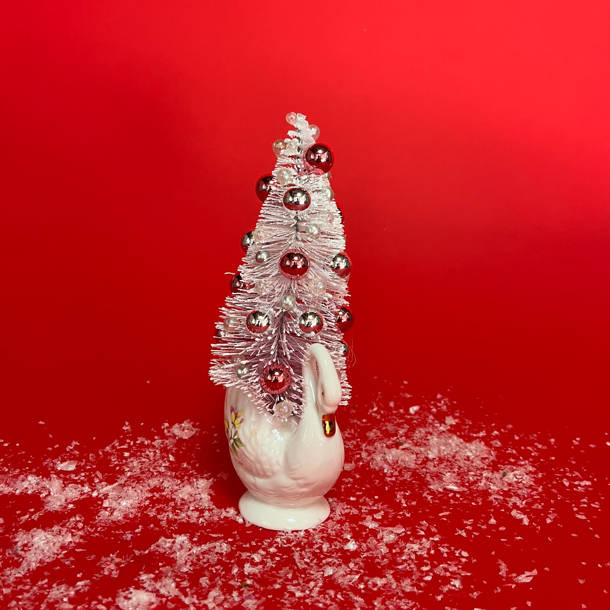 a white floral Vintage Ceramic Swan w/ Flocked Christmas Tree Centerpiece against a red background. 