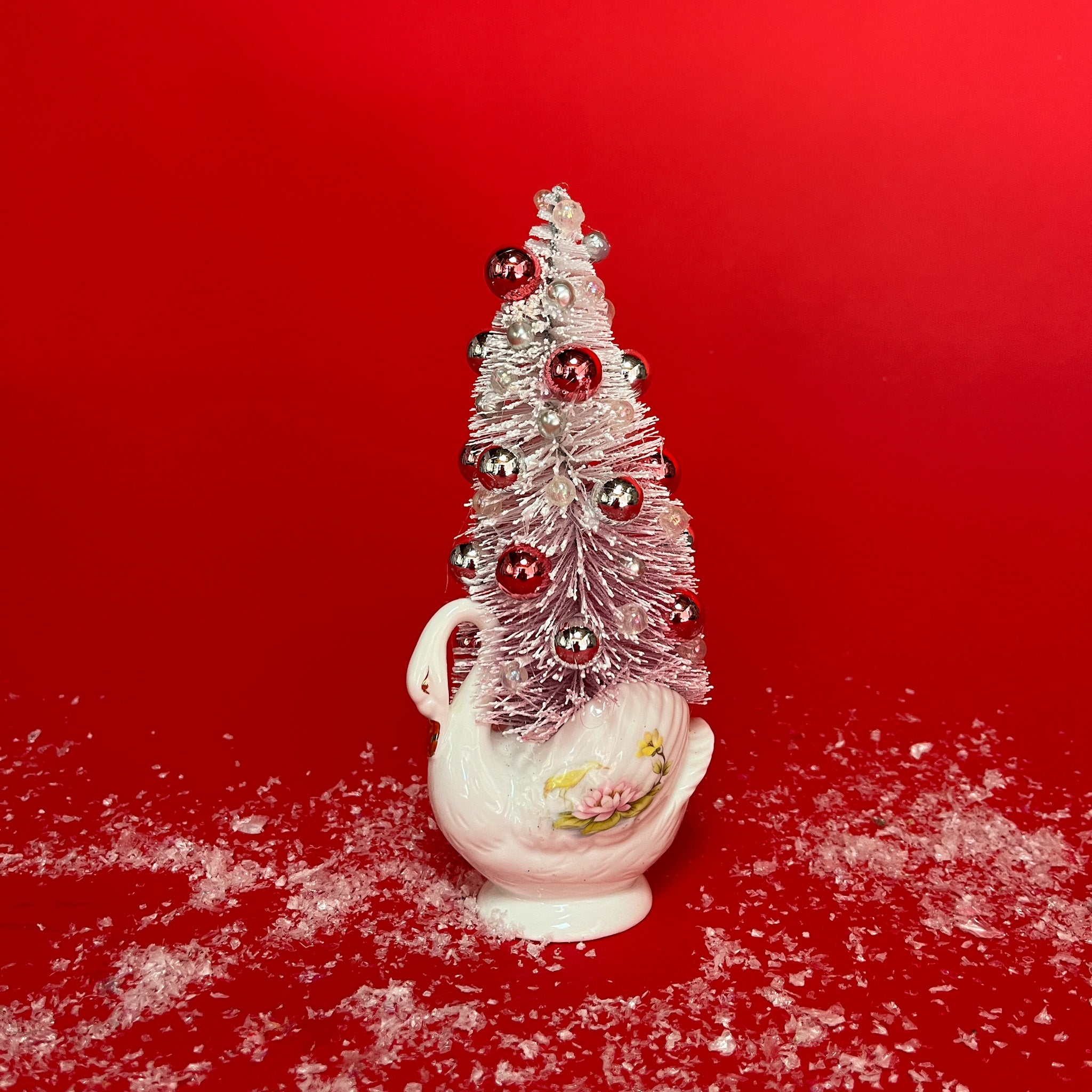 a white floral Vintage Ceramic Swan w/ Flocked Christmas Tree Centerpiece against a red background. 