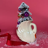 a white Vintage Small Arched-Neck Ceramic Swan w/ Gold/Purple Frosted Christmas Tree inside it against a red background. 