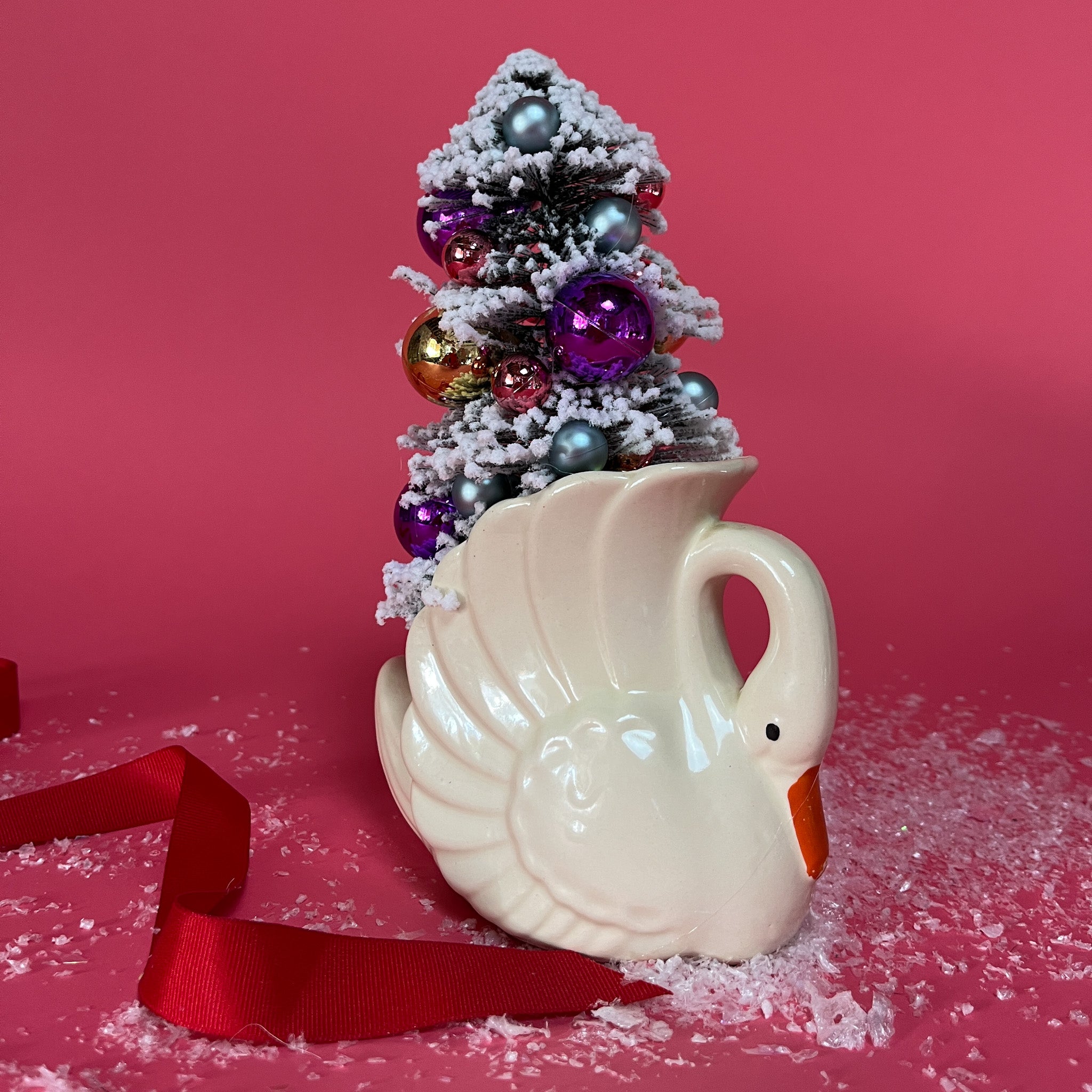 a white Vintage Small Arched-Neck Ceramic Swan w/ Gold/Purple Frosted Christmas Tree inside it against a red background. 