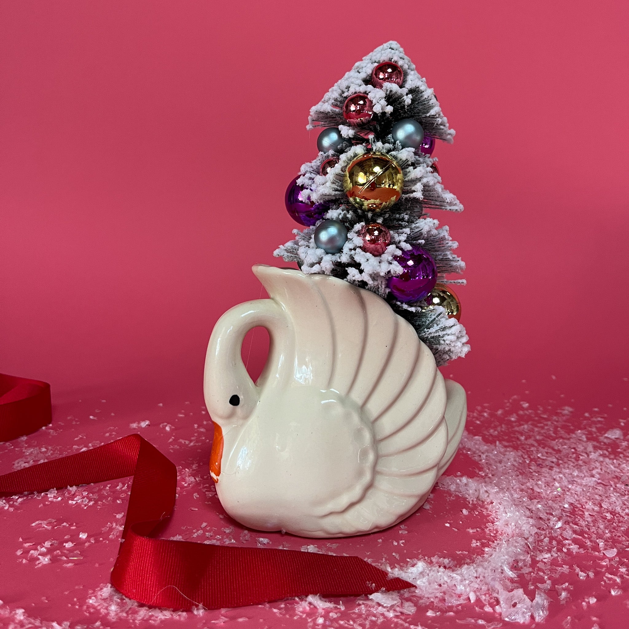 a white Vintage Small Arched-Neck Ceramic Swan w/ Gold/Purple Frosted Christmas Tree inside it against a red background. 