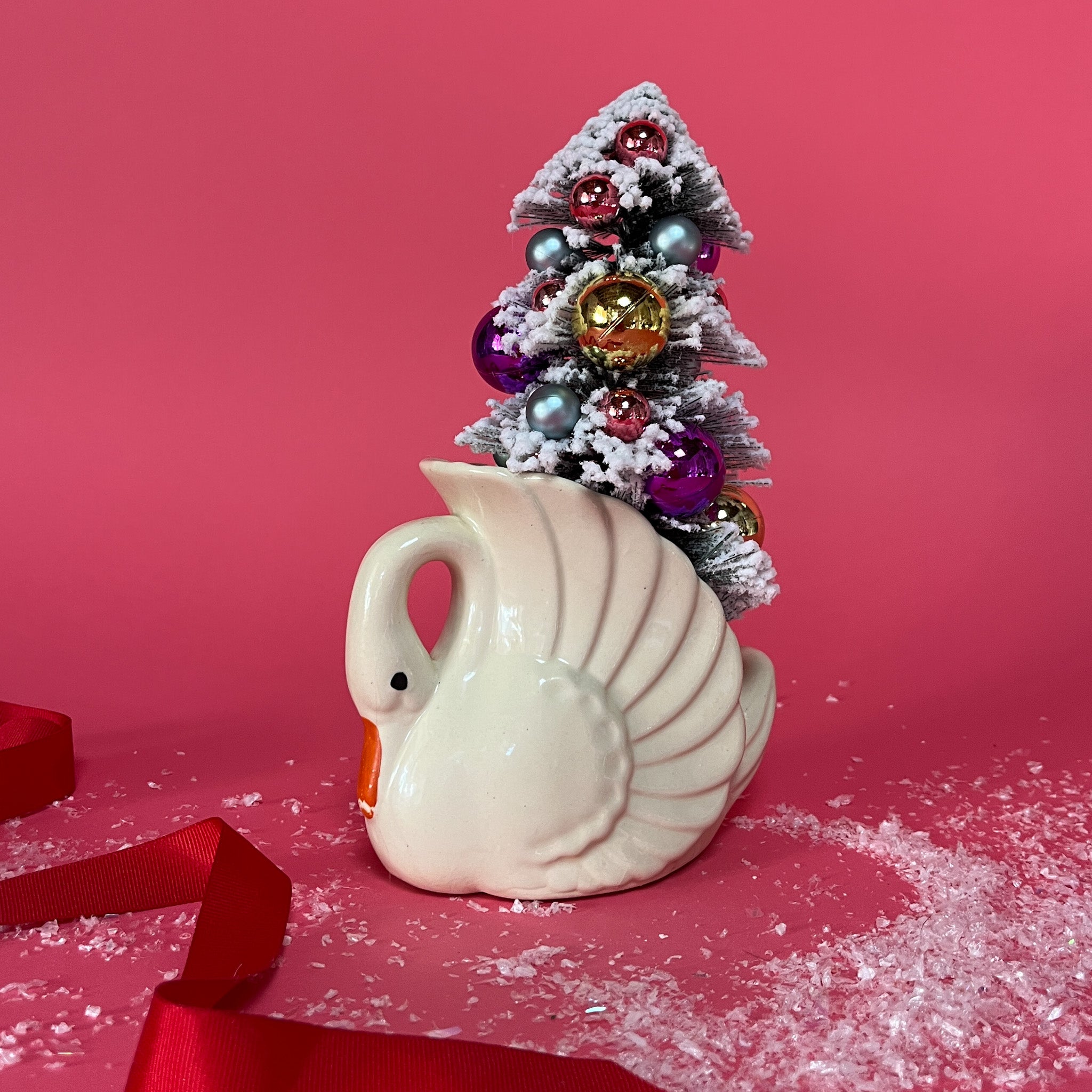 a white Vintage Small Arched-Neck Ceramic Swan w/ Gold/Purple Frosted Christmas Tree inside it against a red background. 