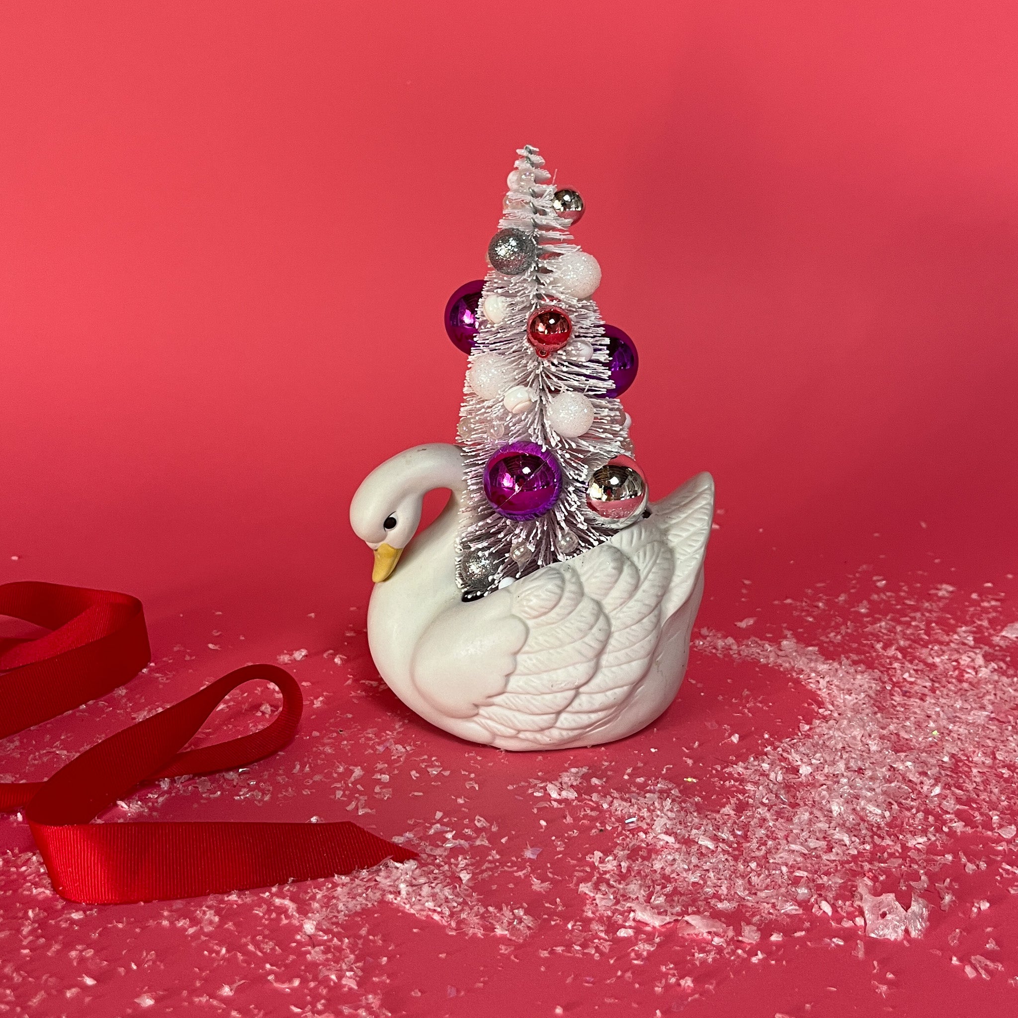 a Vintage Small White Ceramic Swan w/ Pink/Purple Glitter Christmas Tree Centerpiece against a red background