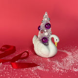 a Vintage Small White Ceramic Swan w/ Pink/Purple Glitter Christmas Tree Centerpiece against a red background