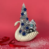 a Vintage White/Gold Ceramic Swan w/ Silver/Blue Glitter Christmas Trees Centerpiece against a red background. 