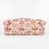 A classic three-seat sofa upholstered in a red and cream toile pattern, set against a plain white studio background.