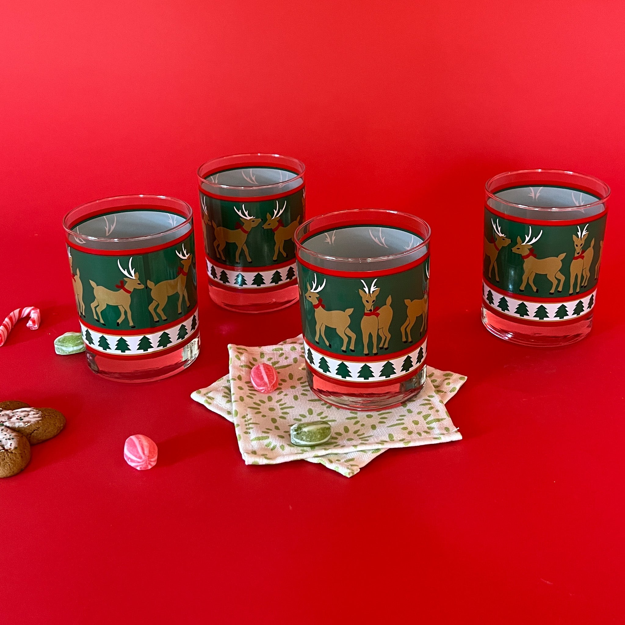 Vintage Prancing Reindeer Drinks Glasses, Set of 4. Reindeer on green background, band of trees on white.