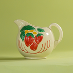 A white vintage strawberry pitcher with strawberry motifs decorating the side.