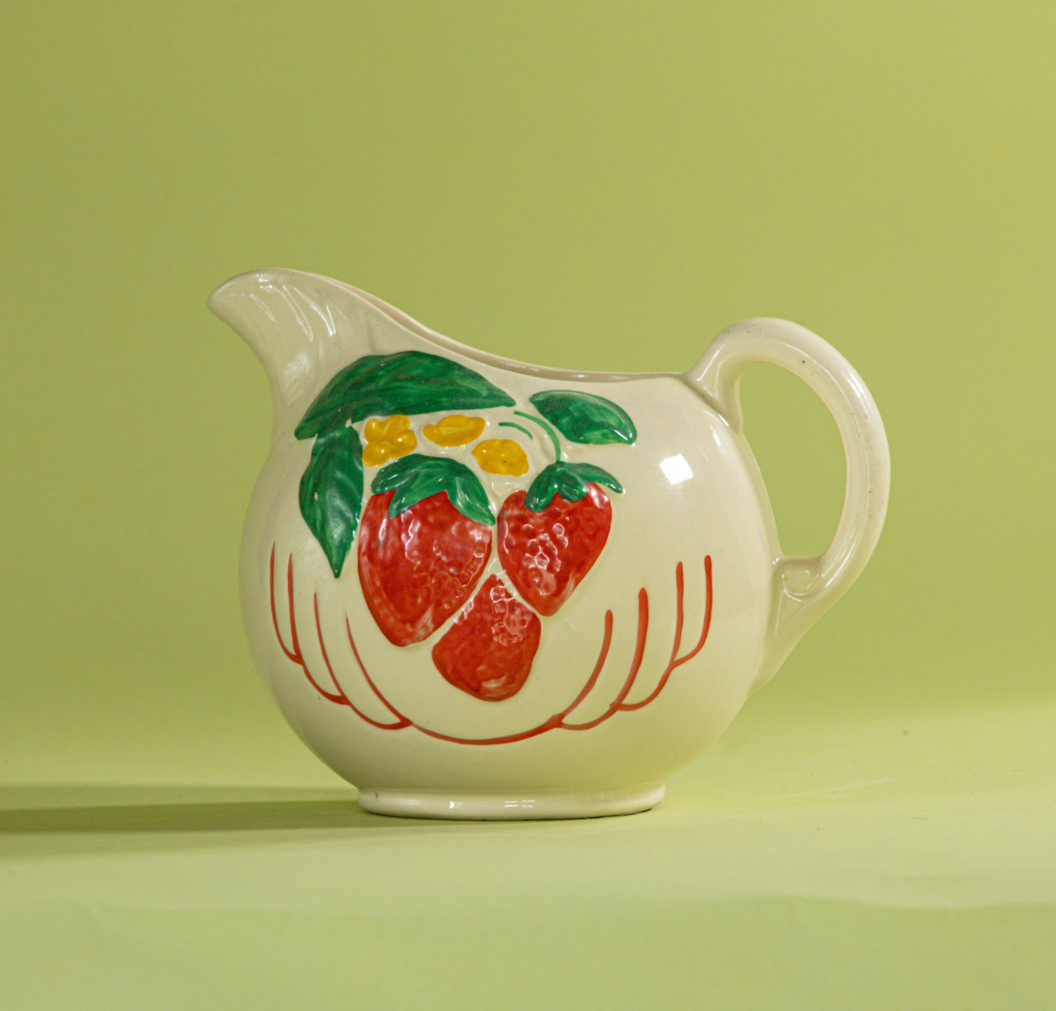 A white vintage strawberry pitcher with strawberry motifs decorating the side.