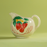 A white vintage strawberry pitcher with strawberry motifs decorating the side.