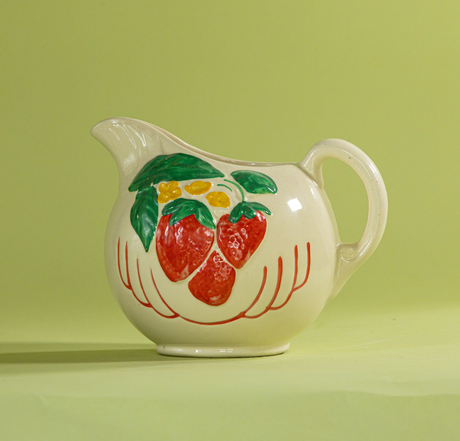 A white vintage strawberry pitcher with strawberry motifs decorating the side.