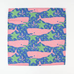 Cloth napkin laid flat with pink whale and green seaweed pattern on a blue background.