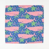 Cloth napkin laid flat with pink whale and green seaweed pattern on a blue background.