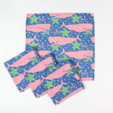 Set of cloth napkins with pink whale and green seaweed pattern on a blue background.